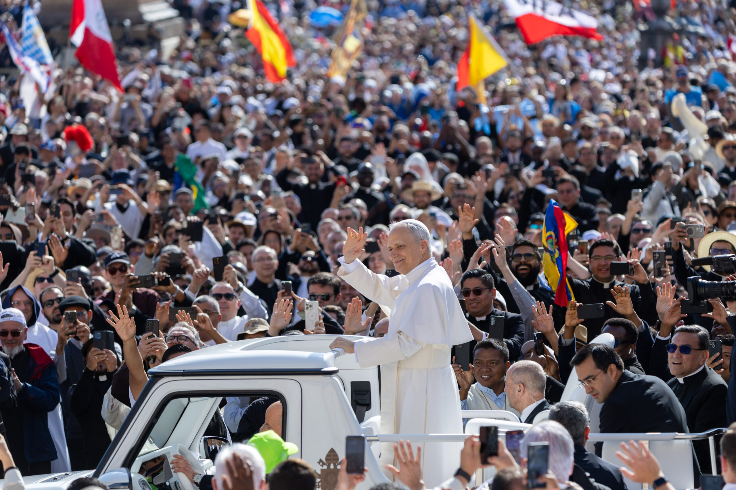 Der neue Papst Leo XIV. steht auf dem Papamobil, umgeben von Menschen und winkt.